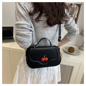 Detail of black matte crossbody bag featuring a 3D red cherry charm and adjustable strap