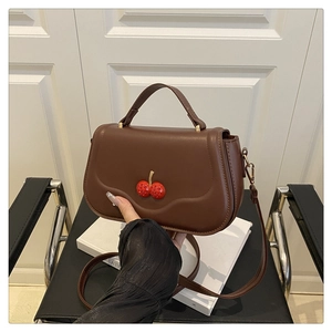 Macro detail of brown leather bag featuring decorative red rhinestone cherry accents