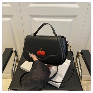 Detailed shot of black crossbody bag with red rhinestone cherry charm and gold hardware