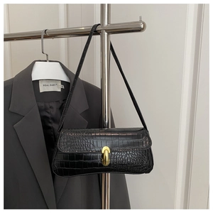 Detail of black crocodile texture shoulder bag with gold U-shaped buckle on a suit jacket