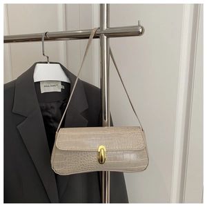 Close-up of beige crocodile pattern handbag with gold clasp on a minimalist clothes rack
