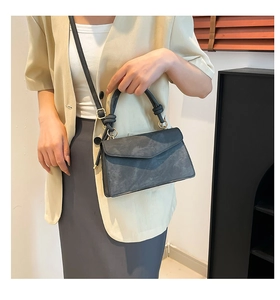 Detail of dark grey suede crossbody bag with V-shaped flap and knotted handle