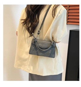 Detail of dark grey suede crossbody bag with knot handle worn by a model in interior