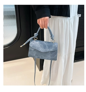 Detail of blue textured mini crossbody bag with knotted handle and golden metal ring