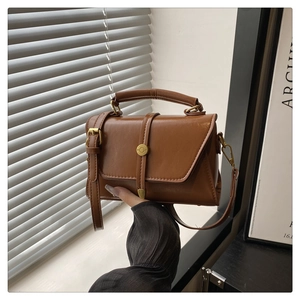 Detail van een bruine leren crossbodytas met gouden sluiting tegen een moderne achtergrond