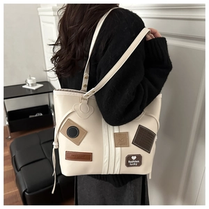 Detail of cream white tote bag with patchwork leather motifs worn over a black sweater