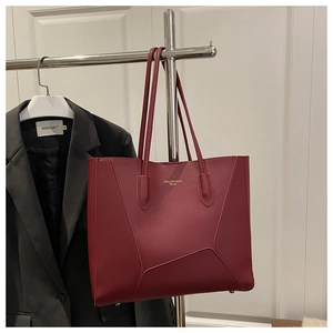 Detail of burgundy tote bag showing geometric stitching and gold logo on the leather