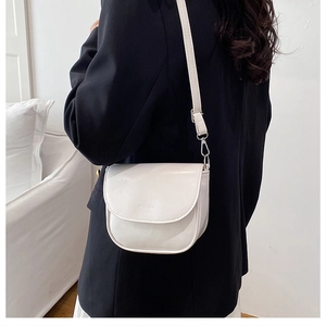 Dettaglio di una borsa a sella crema minimalista con tracolla regolabile indossata