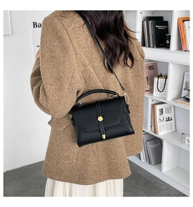 Detail of black pebbled leather crossbody bag with gold hardware on a brown blazer model