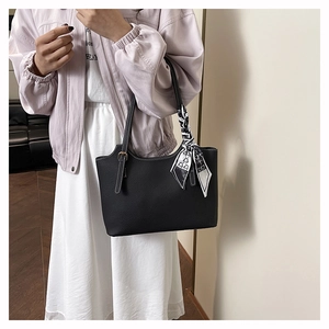 Dettaglio borsa tote in pelle nera a grana con elegante foulard di seta sul manico