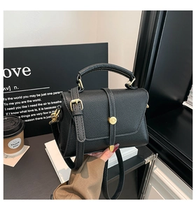 Close-up of black lychee grain leather handbag with gold metal lock and top handle