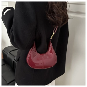 Détail du sac croissant en cuir verni bordeaux brillant porté sur l'épaule