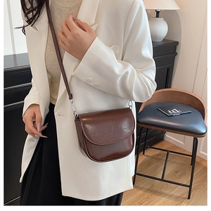 Détail du sac besace en cuir marron foncé avec boucles argentées sur un blazer blanc chic