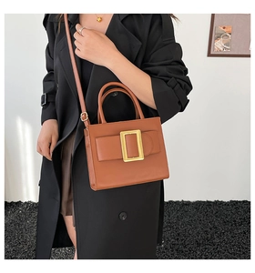Detail of caramel leather shoulder bag with large gold buckle on black trench coat