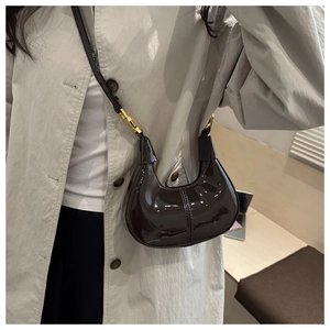 Détail du sac croissant marron foncé brillant avec boucle dorée et couture verticale