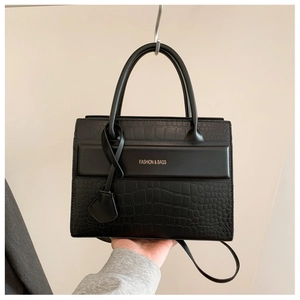 Détail d'un sac à main noir à texture crocodile avec lettrage doré et poignée