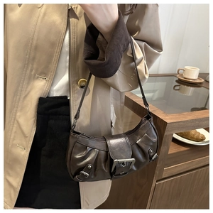 Detail of dark brown pleated hobo bag with silver buckle worn with a beige trench coat