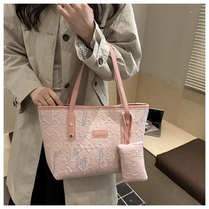 Detail of pink quilted tote bag with embroidery, brand plaque, and matching charm pouch