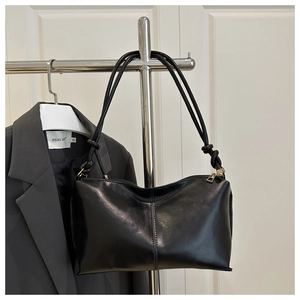 Détail du sac baguette en similicuir noir avec nœud de bandoulière et zip doré brillant