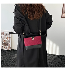 Detailed close-up of a burgundy suede and black leather bag with a gold metal V logo