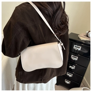 Close-up of minimalist cream white underarm bag with smooth glossy finish on shoulder