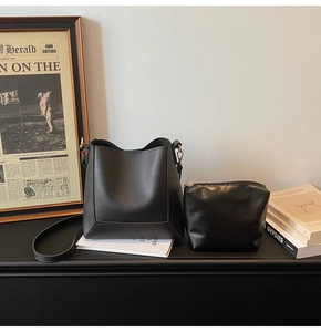 Detail of minimalist black leather bucket bag and pouch set on a vintage desk