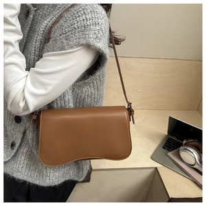 Detail of caramel shoulder bag with wave base on a minimalist desk with office props