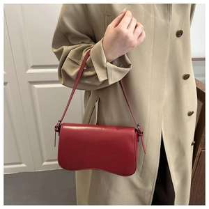 Glossy red leather underarm bag with unique wave-shaped bottom worn with a beige coat