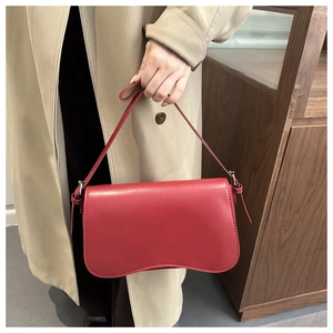 Detail of red leather shoulder bag with sleek curved bottom and chic knotted strap accent