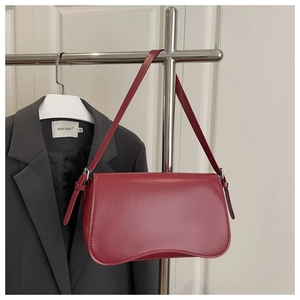 Close-up of a burgundy shoulder bag with a unique wavy base and adjustable strap