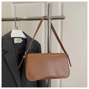 Close-up of brown leather baguette bag with adjustable strap on a garment rack