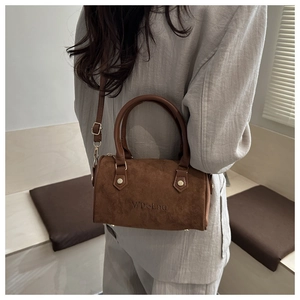 Gros plan du sac Boston en daim marron avec logo embossé et détails de texture premium