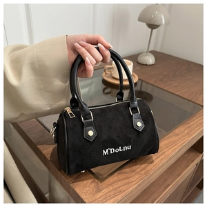 Détail du sac Boston en daim noir avec logo blanc et ferrures dorées élégantes