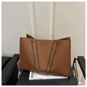 Detail of a large brown tote bag with metal chain strap and pebble leather texture