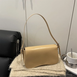 Minimalist beige underarm bag with unique wavy base design on a cozy knit fabric background
