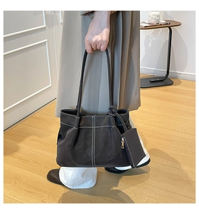 Close-up of brown suede tote bag featuring white contrast stitching and mini pouch detail