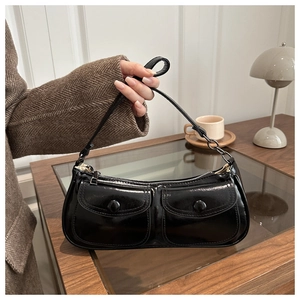 Detail of glossy black baguette bag featuring dual front pockets and metal chain strap accent