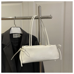 Detail of off-white shoulder bag with knot bows and silver logo against black blazer