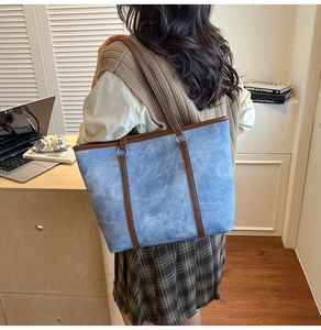 Détail d'un sac cabas en denim avec anses en cuir marron et anneaux dans un décor de bureau