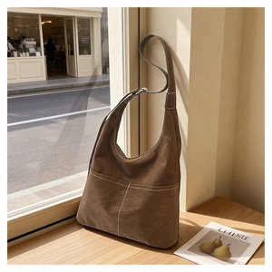 Close-up of brown suede hobo bag with white contrast stitching and adjustable strap