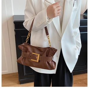 Détail du sac nuage plissé marron avec bandoulière en chaîne dorée sur blazer blanc
