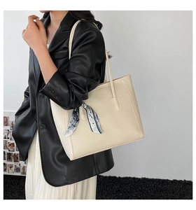 Detail of a creamy white leather tote bag with a blue printed silk scarf tied on the handle