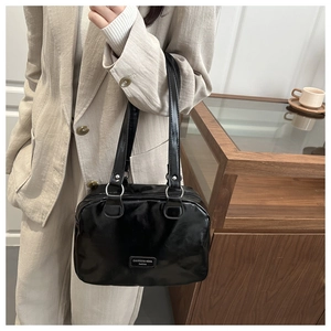 Dettaglio della borsa nera lucida indossata da una modella in abito beige chic