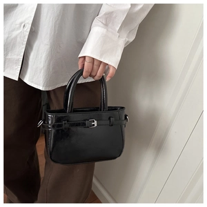 Close-up of glossy black leather handbag showing metallic buckle and mirror-like texture