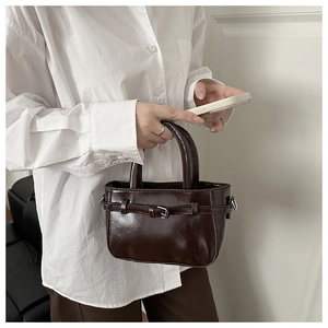 Close-up of a vintage dark brown glossy leather handbag with belt buckle detail and handle