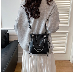 Detail of black bucket bag with silver chains and drawstring closure on a model