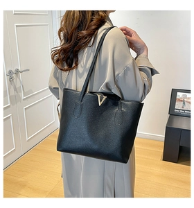 Detail of black pebbled leather tote bag featuring a golden V-shaped metal logo ornament