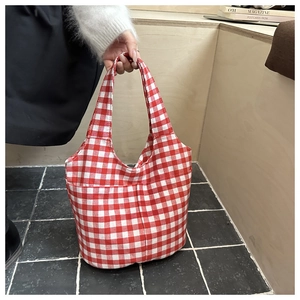 Detail of red and white plaid canvas tote bag held by a model in a minimal setting