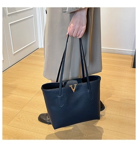 Detail einer schwarzen Leder-Tote-Bag mit Narbenleder und auffälliger goldener V-Schnalle