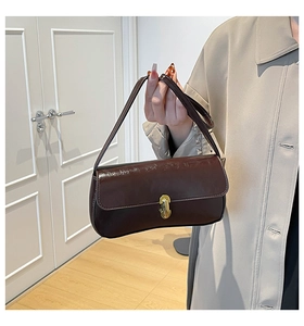 Detail einer dunkelbraunen Lackledertasche mit Goldverschluss und dünnem Trageriemen